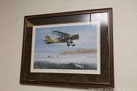 Framed print showing a vintage airplane flying over a misty field with buildings in background.