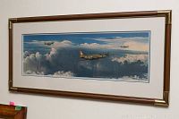 Framed panoramic print showing three WWII aircraft flying above clouds in a blue sky.