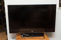 Front view of LG 42 inch TV on stand with remote placed on stand, showing some wear on edges.