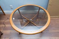 Top view showing round glass tabletop with clear wooden rim and underside X-shaped wooden support.