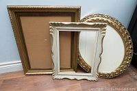 Three large decorative picture frames arranged against a wall on a hardwood floor, showing frame details and finish.
