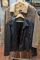 Two leather jackets hanging on wooden hangers. One black Danier jacket and one tan AE Sport and Co jacket with shearling lining.