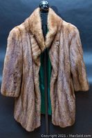 Front view of vintage mink fur coat on stand under black backdrop showing full length, light brown color with collar and opening.