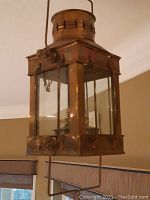 Side view of brass nautical lantern showing rectangular shape, top vent, glass panels and hanging handle.