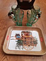 Four green Coca-Cola glass mugs with handles placed behind a rectangular Coca-Cola serving tray on wooden floor.