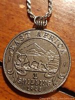 Close-up front side of the coin pendant showing a lion and Mount Kilimanjaro with text 'EAST AFRICA 1 SHILLING 1948'