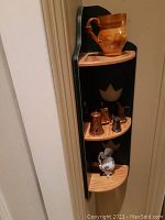 Side view of the wooden corner shelf with vintage brass, copper, and ceramic decor items on three shelves