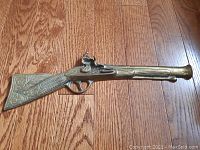 Top view of the brass blunderbuss wallhanger showing detailed engravings on the stock and barrel, laid on a wooden floor.