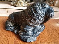 Side view of black stone walrus sculpture signed by Clement Dube on base left side.