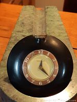 Close front view of black bakelite circular ladies purse clock with gold-tone metal accents and white dial with Arabic numerals.