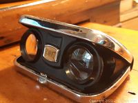 Vintage Fisher-Dietz folding binoculars closed showing chrome edges and black center with logo badge.