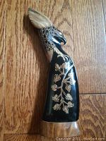 Side view of carved bull's horn eagle showing head, neck, and engraved leafy design on body.