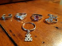 Group of five vintage ladies silver rings displayed on a wooden surface showing different designs and stones.