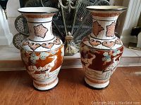 Pair of vintage ceramic vases with decorative crane and floral motifs on hardwood floor in front of mirror.