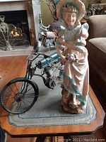 Side perspective of the antique bisque porcelain lady figurine on a small table in a living room. Fireplace and other furniture visible in background.