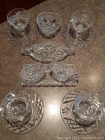 Top-down view of the crystal serving set arranged on a table showing dessert plates with saucers, creamer set on tray, pickle dish, and candy dish.