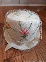 Front view of vintage white ladies hat with embroidered pink, blue, yellow flowers and decorative netting