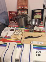 Full view of the canning supplies lot arranged on a multicolored striped tablecloth showing pot, strainer, cookbooks, canning jars, chopping board and utensils