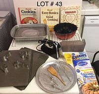 Photo showing Hamilton Beach handheld mixer with two beaters, various metal baking pans and trays, wooden spatula, metal cooking racks, and six cookbooks mostly about baking and cooking.