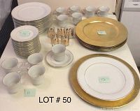 Fairfield Classic Gold fine white china plates, cups, saucers, gold chargers, and glass candle holders displayed on table with lot number.