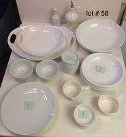 Photo showing large oval serving trays with handles, large round bowls, small round bowls and coasters, small spouted bowls, and large round plates arranged on table.