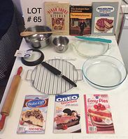 Photo showing baking and cooking items including glass pie pans, stainless steel mixing bowls, wooden rolling pin, metal cooling rack, springform pan, pie server, and 6 cookbooks