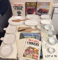 Photo showing complete baking and cooking set arranged on a white table. Includes white ceramic dishes and bowls in various shapes and sizes, wooden spatula, rectangular cutting board with a knife, and multiple vintage McCall's cookbooks standing upright at the back.