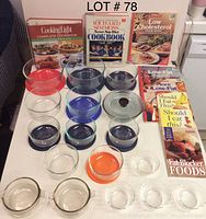 Photo showing a variety of Pyrex glass bowls in different sizes and colors, some with lids, and eight cookbooks standing upright behind them.