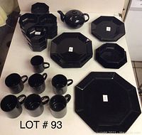 Photo of black octagonal dishes including plates, bowls, cups, and a teapot arranged on a table.