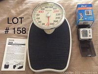 Taylor Professional mechanical scale with large 8.5-inch dial, instruction manual, ReliOn blood pressure cuff with digital display and box, all items visible on table.