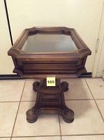 Front view of the wooden curio table showing glass top and carved pedestal base