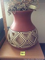 Full view of terra cotta lamp with coiled electrical cord on top and geometric patterned lower body.
