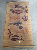 Natural fiber mat with multiple stylized fish painted in various colors on a woven surface.