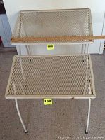 Top view of two metal outdoor side tables stacked, showing diamond mesh tops and folding legs with some rust and paint wear.