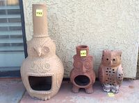 Photo of two clay chimeneas and one clay owl candle holder placed outdoors against a beige wall.