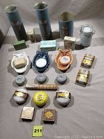 Photo showing three owl-shaped ceramic soap dishes in white, blue, and orange, three cylindrical owl-decorated candles, and multiple assorted soaps including bar soaps, round soaps, and boxed soaps arranged on a white surface.