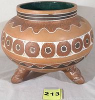 Full side view of the terra cotta planter showing carved geometric patterns and wavy lines, three legs, and green glazed interior.