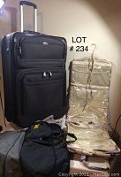 Large black rolling suitcase, clear garment bag, gray nylon duffle, and two small black accessory bags arranged together
