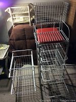 Photo showing three white painted metal wire storage units with various wire racks and two plastic bins placed inside one of the units.