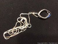 Sterling silver necklace pendant lying flat on black fabric background showing the diamond-embedded hollow rounded square shape.