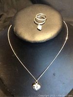 Sterling silver necklace with heart pendant displayed with two silver rings, one featuring a dangling heart charm.