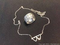 Sterling silver necklace with two connected open hearts shown laid out on black surface.