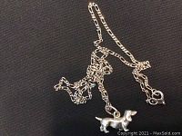 Sterling silver chain with dachshund pendant laid on black fabric background, showing the pendant and chain details