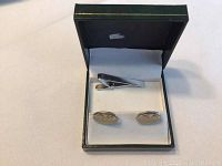 Set shown in green jewelry box with white interior, including two oval silver cuff links and a tie pin.