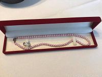 Freshwater pink pearl necklace laid inside red velvet-lined jewelry box showing the sterling silver clasp and the silver band ring inside the box.