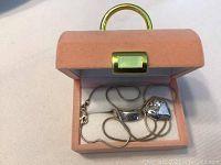 Open pink jewelry box showing the silver necklace chain and ring inside