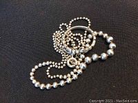 Photo of sterling silver beaded necklace and matching ring placed on a black fabric background, showing the overall look and silver bead design.