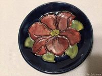 Top view of Moorcroft blue dish showing red hibiscus flower and green leaves on dark blue background