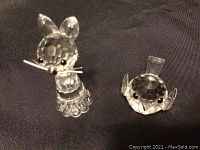 Two Swarovski crystal figurines photographed on a black fabric background; cat figurine levitating with ears and whiskers, bird figurine round and faceted.