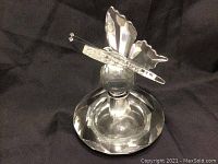 Crystal perfume bottle with butterfly-shaped stopper displayed on a black background, showing front angle revealing faceted design and butterfly details.